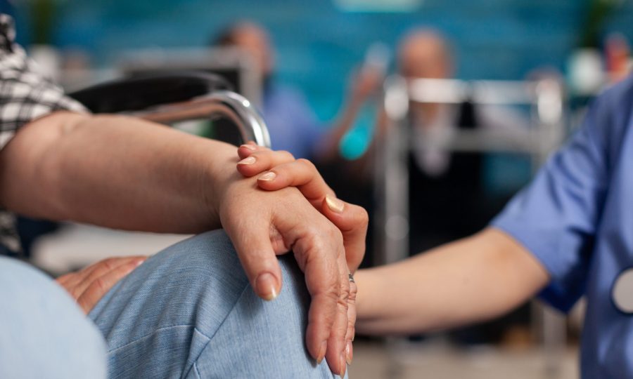 Social assistant worker consoling handicapped pensioner patient touching hands during homecare service. Healthcare support assistance. Social services nursing at home. Caregiver nurse